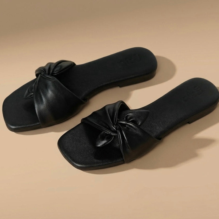 Pair of black slides with bow details on a beige background