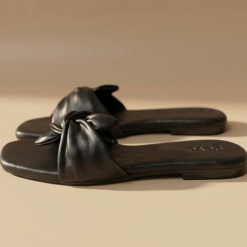 Pair of black sandals with a bow on a beige background