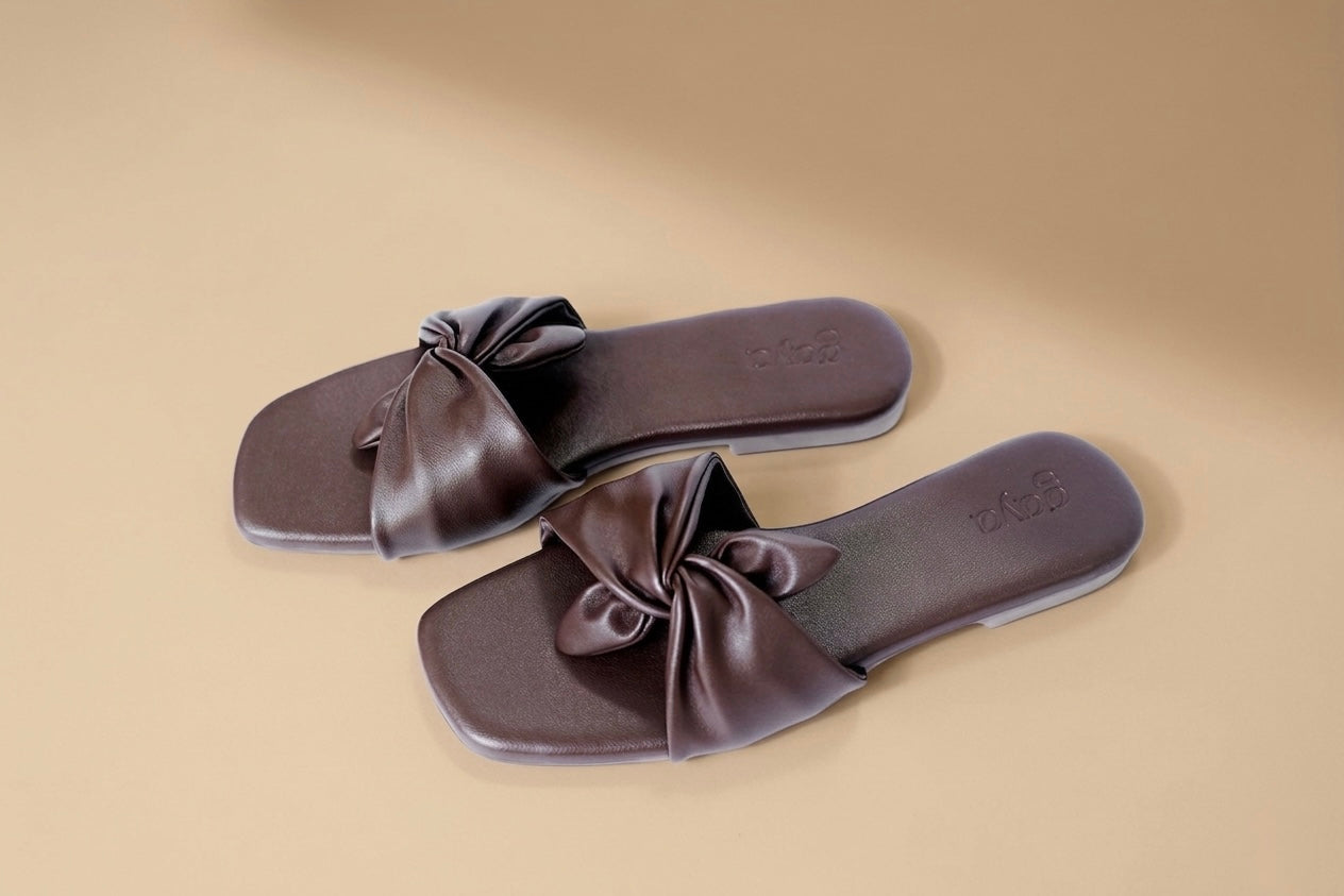 Pair of brown sandals with bow details on a beige background