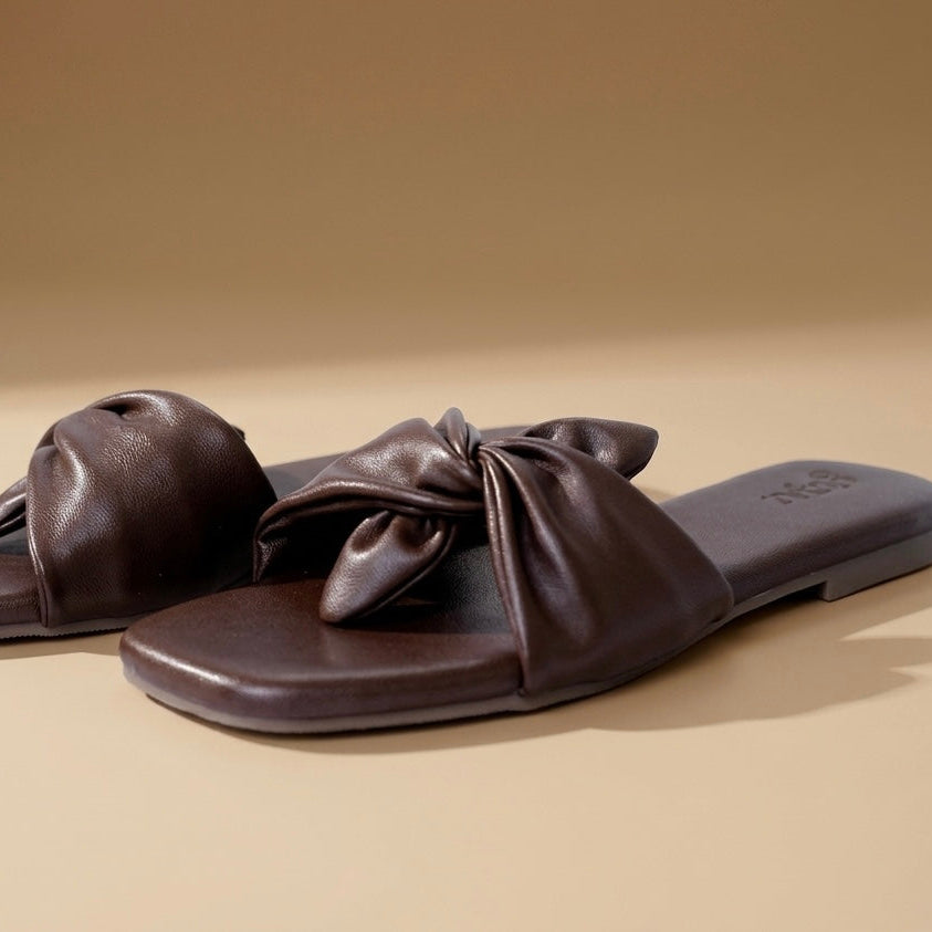 Pair of brown leather sandals with bow details on a beige background