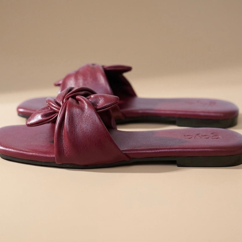 Pair of maroon sandals with a bow on a beige background