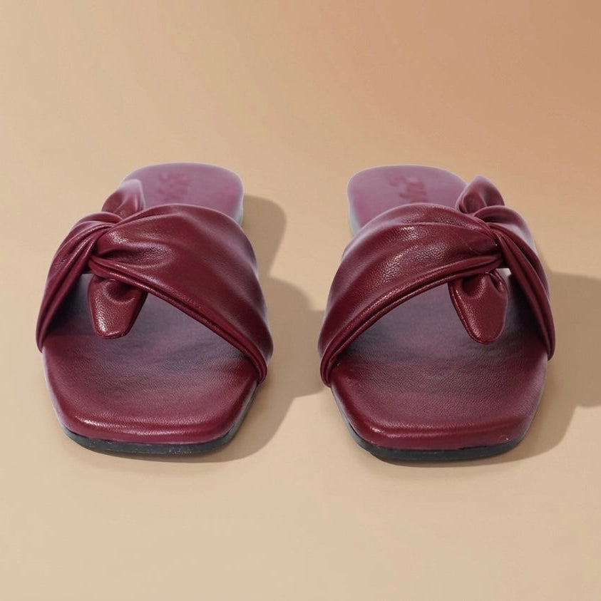 Pair of maroon sandals with a knot design on a beige background