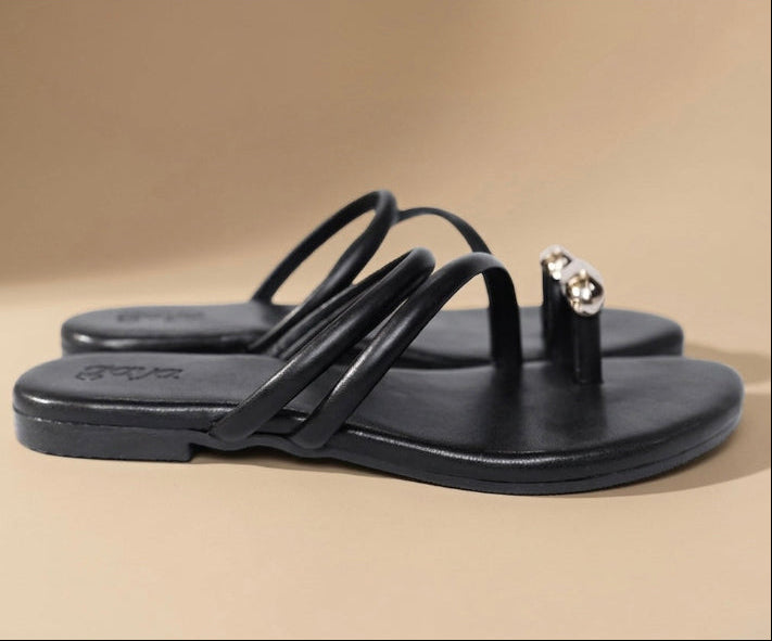 Black sandals with a decorative strap on a beige background