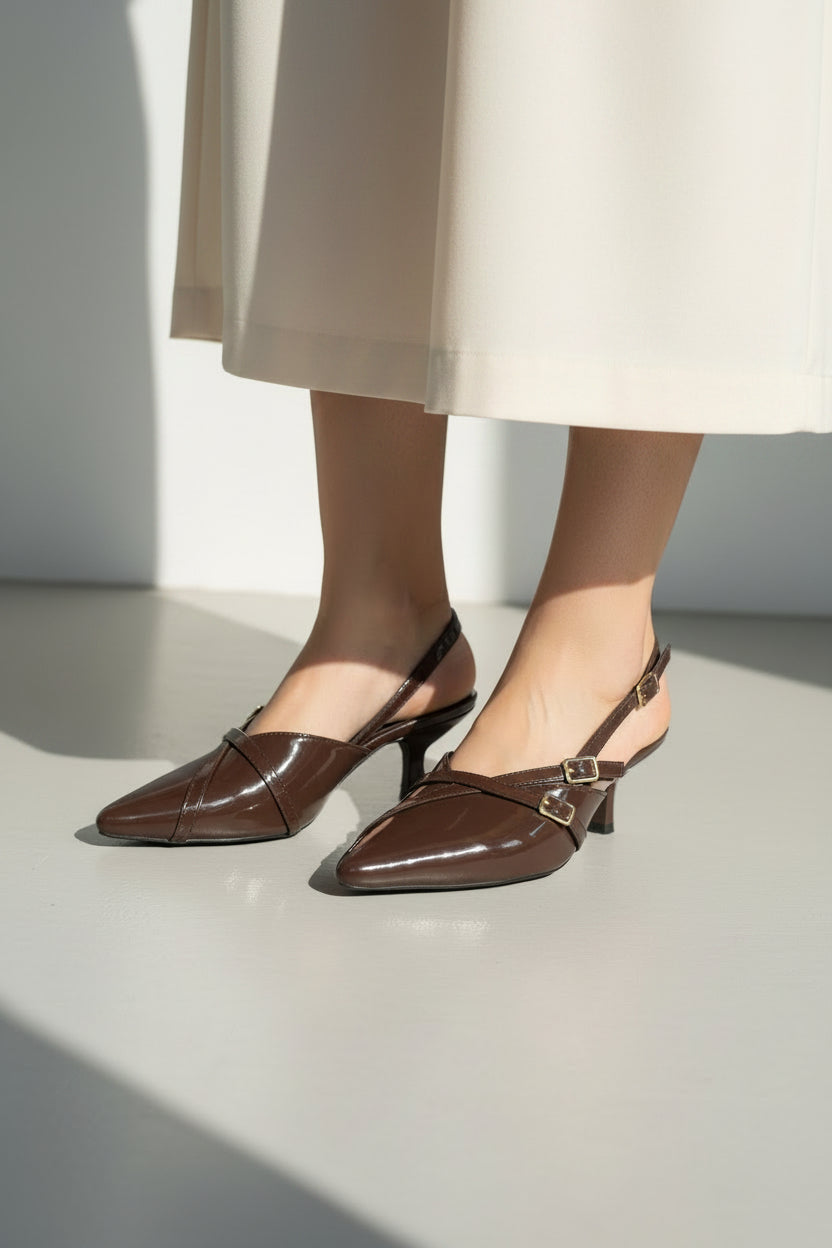Pair of brown high-heeled shoes with gold buckles on a white surface.